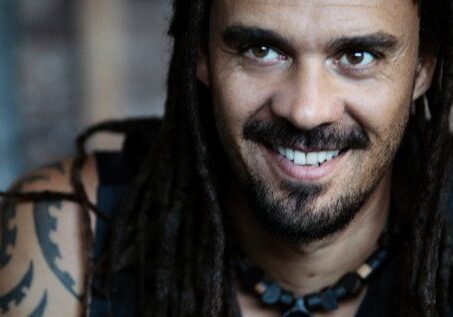 Smiling person with dreadlocks and tattoos.