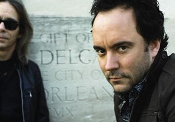 Two men posing in front of stone background.