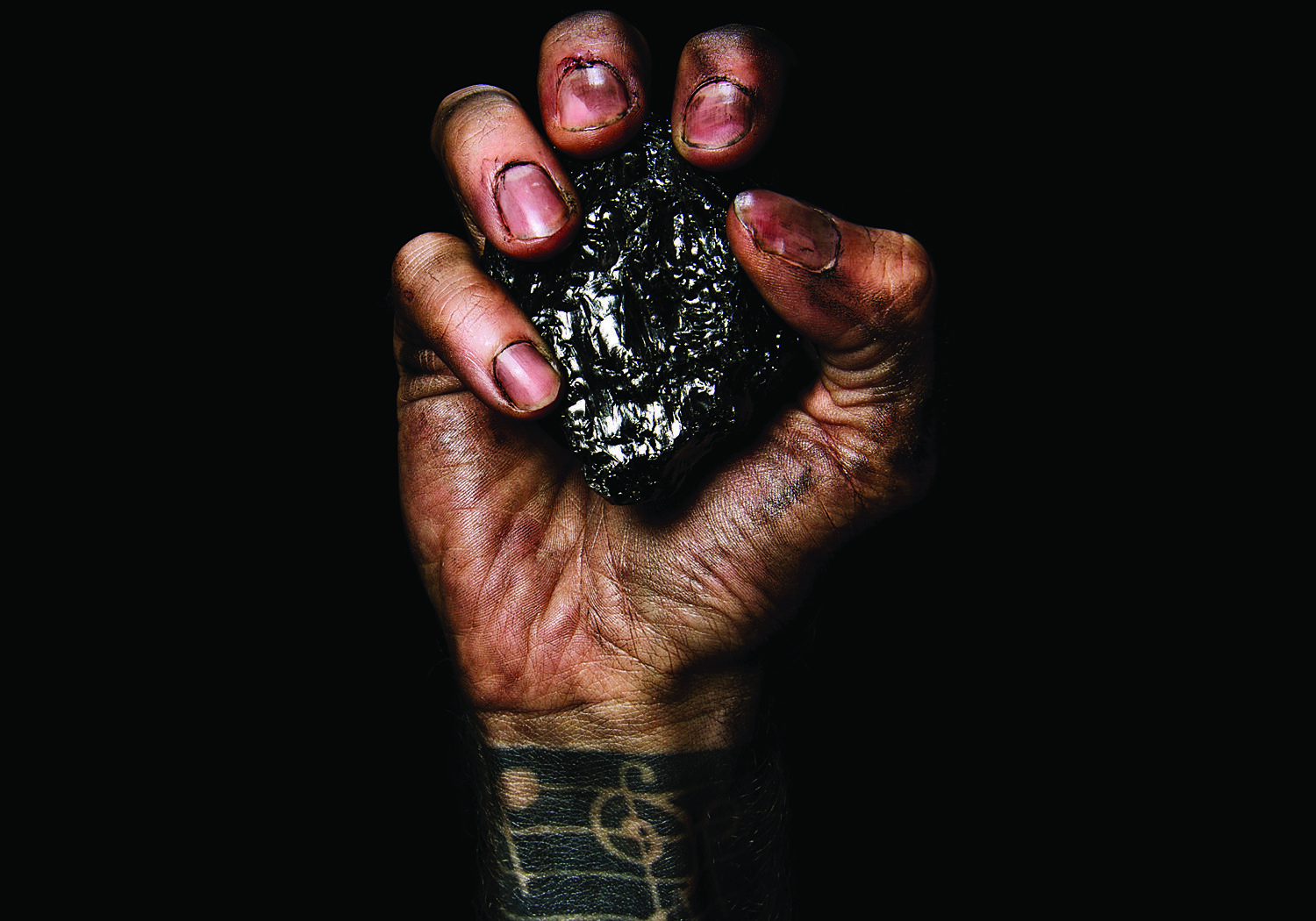 Tattooed hand gripping a piece of coal.