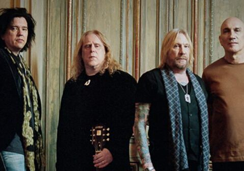 Four men standing in a row indoors.