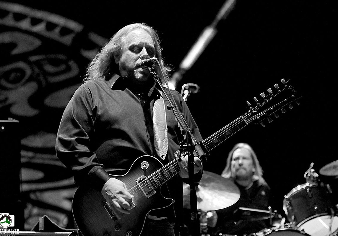 Musician playing guitar on stage, black and white.