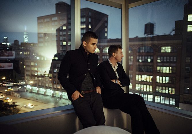 Two men gazing out cityscape window.