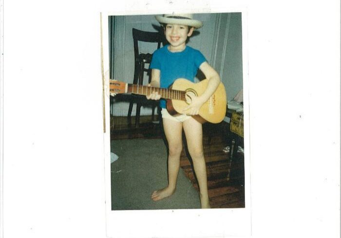 Child playing guitar wearing cowboy hat indoors.