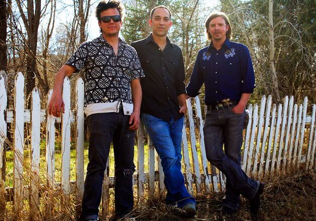 Three men standing by a white fence.