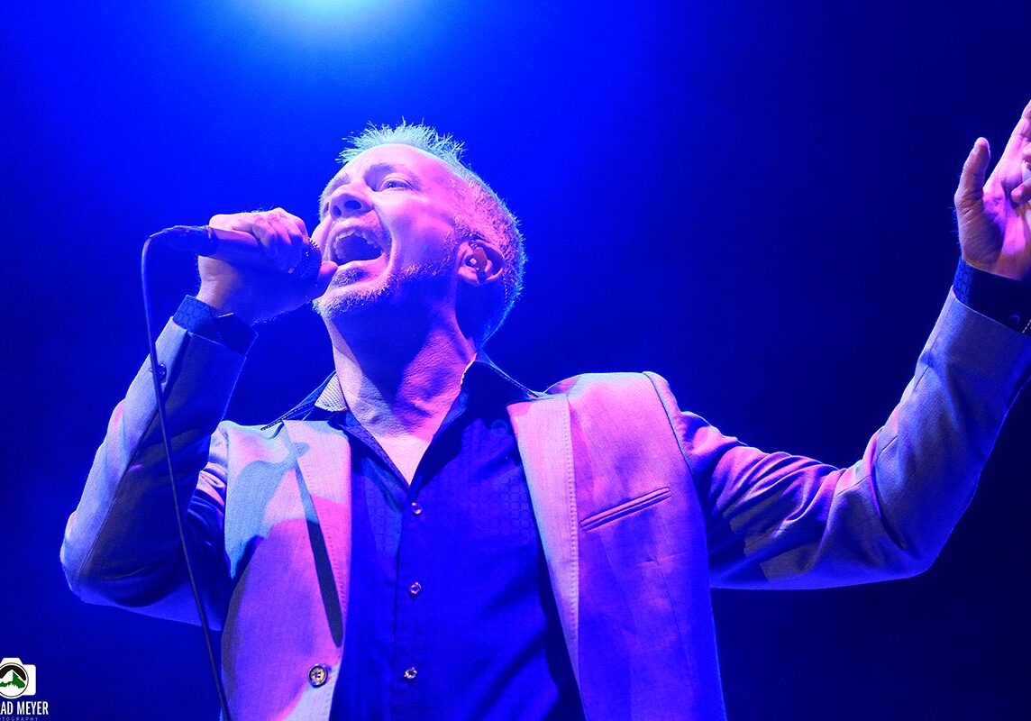 Singer performing energetically on stage, blue lighting.