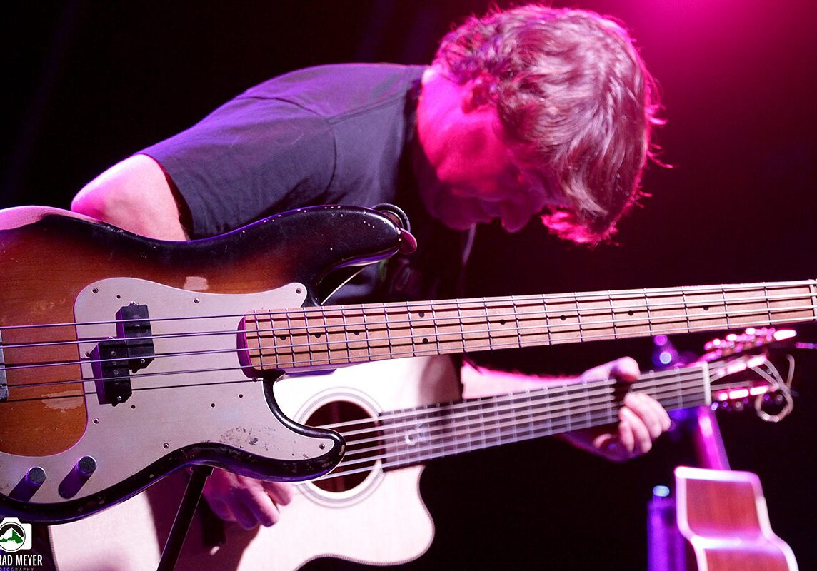 Musician playing bass guitar under purple lighting.
