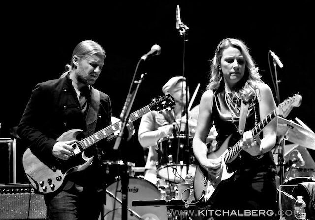 Musicians performing live with guitars on stage.