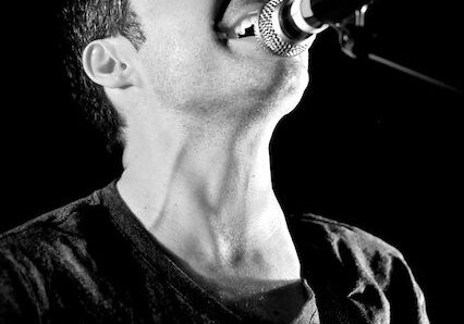 Singer passionately performing on stage, black background.
