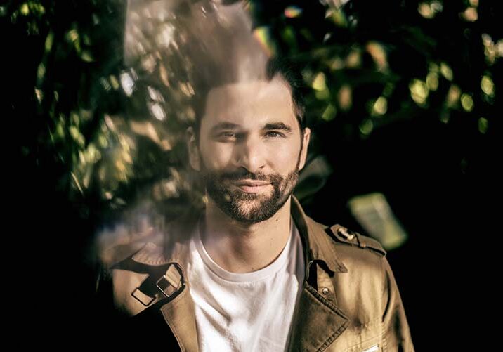 Man smiling in dappled sunlight, outdoors.