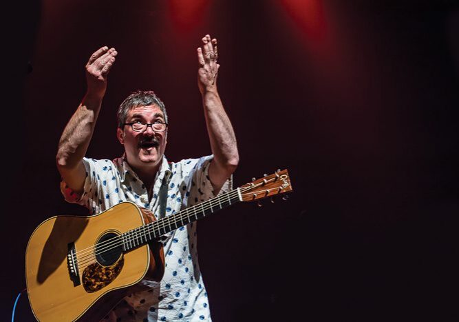Man on stage with acoustic guitar, performing.