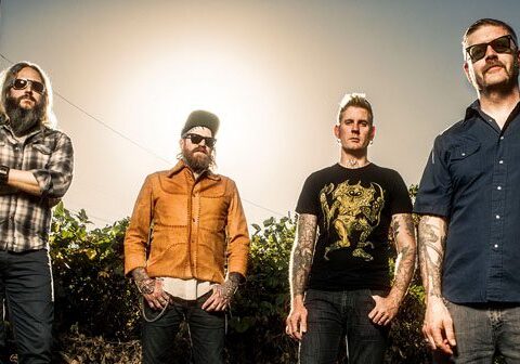 Four men standing outdoors in sunlight.
