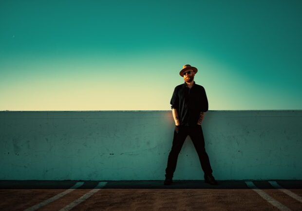 Man in hat standing against turquoise sky.