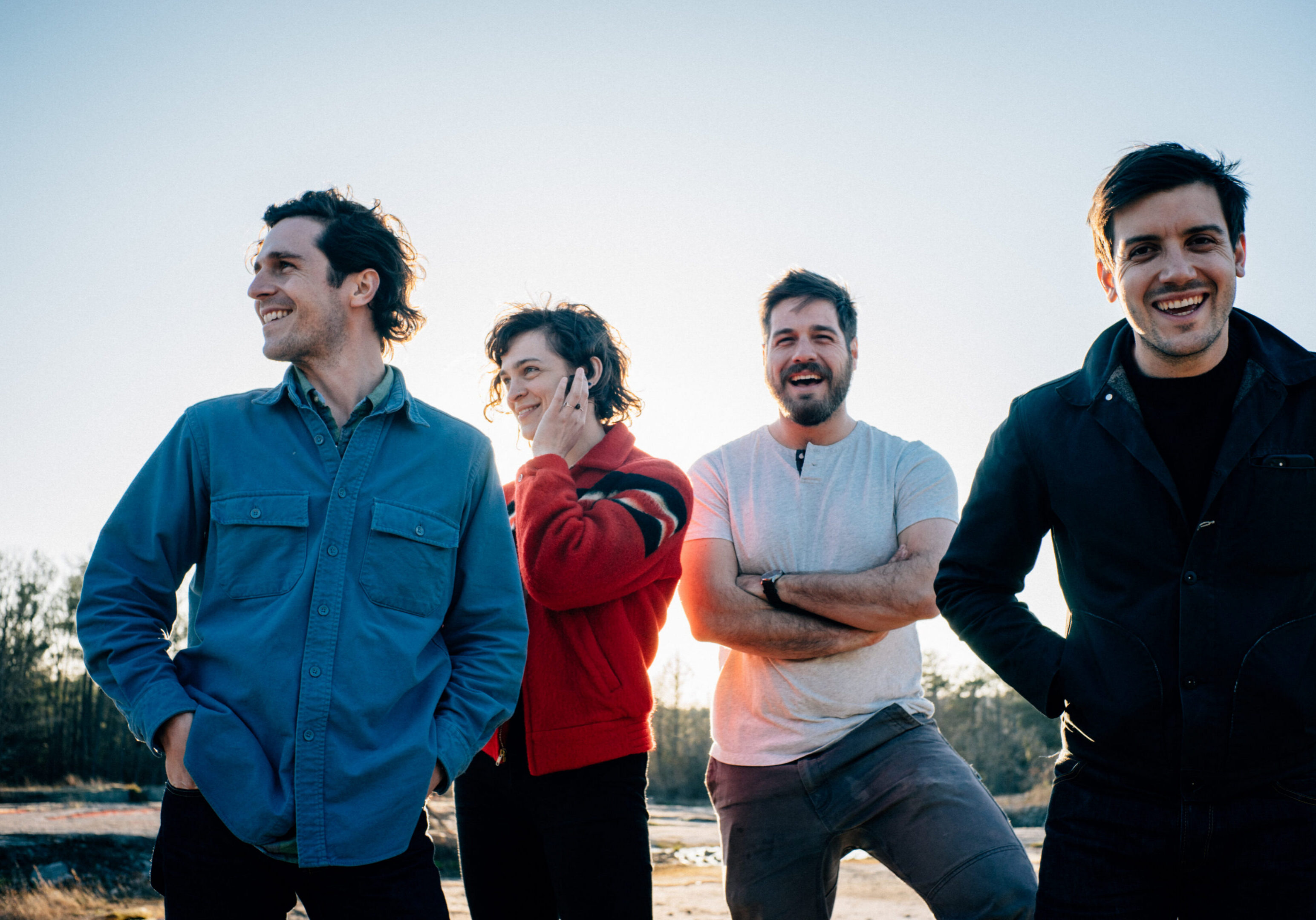 Four men smiling outdoors in daylight.