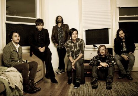 Six people sitting and standing in room.