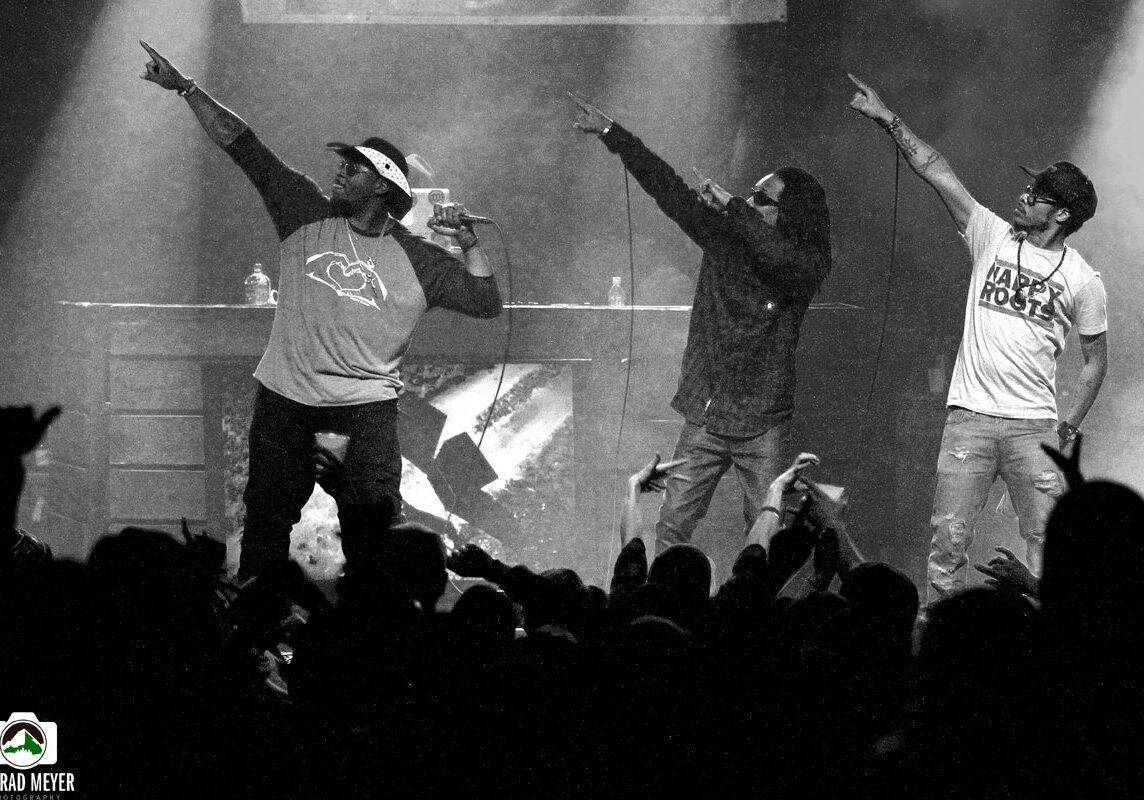 Three performers on stage pointing upward.