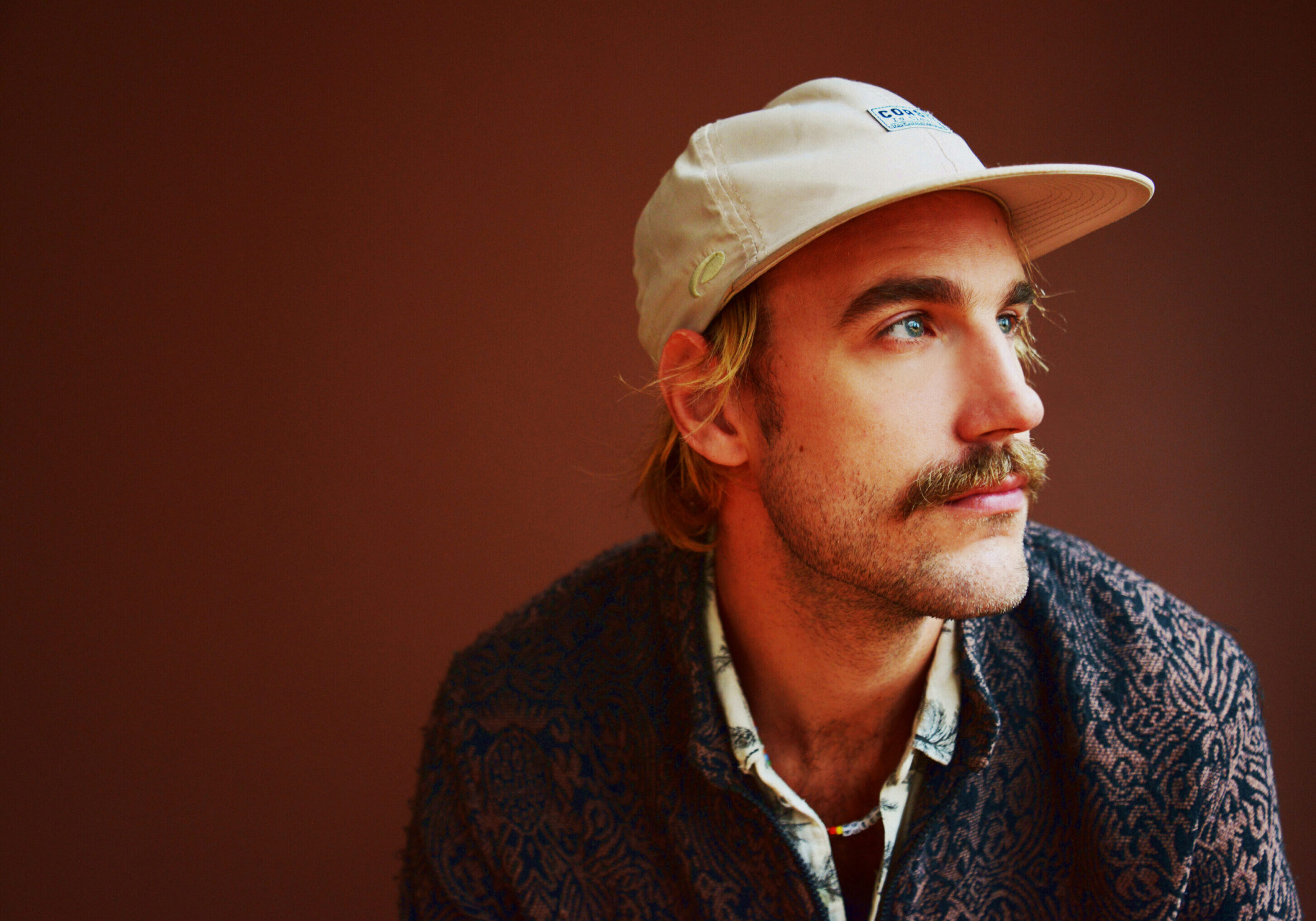 Man wearing cap and patterned shirt, looking sideways.