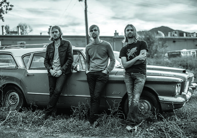 Three men leaning on vintage car outdoors.