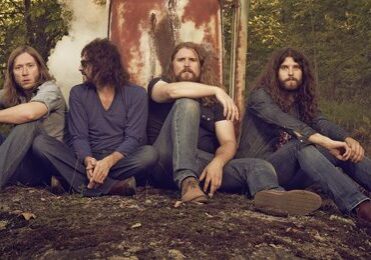 Four men sitting in a wooded area.