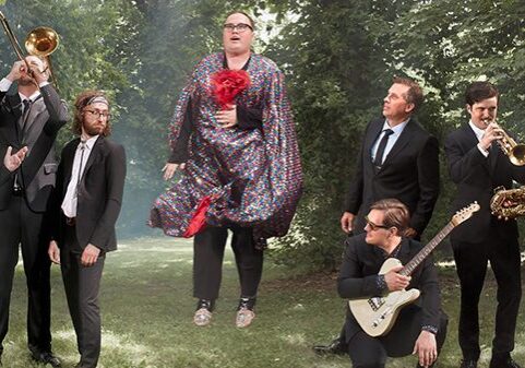 Band posing outdoors with musical instruments.