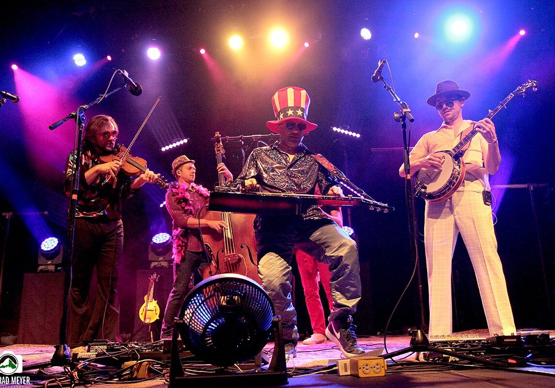 Band performing energetically on stage with instruments.