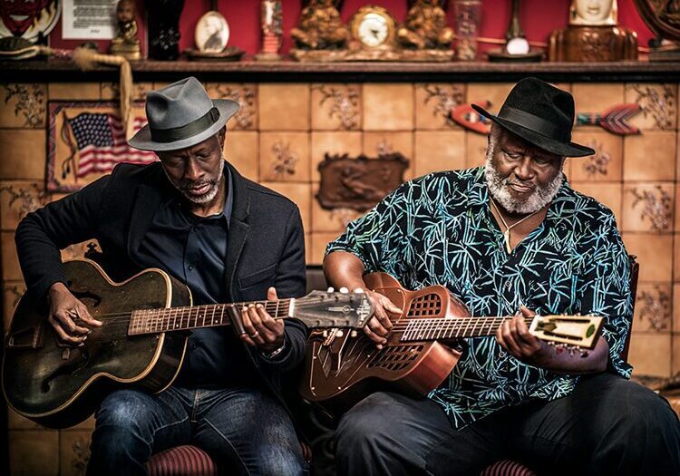 Two men playing guitars in a room.