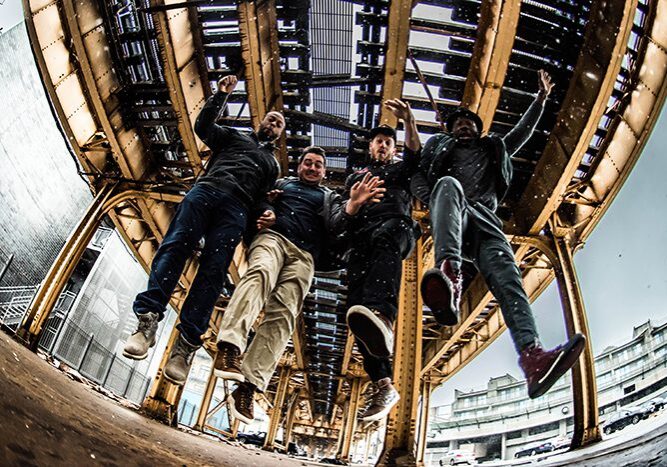 Four people jumping under a metal structure.