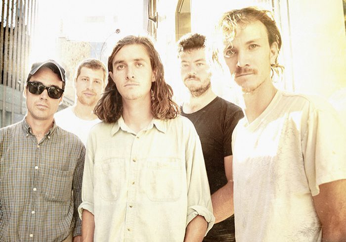 Five men standing in bright sunlight.