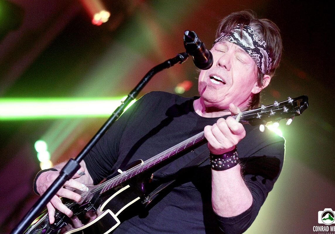 Musician passionately playing guitar on stage.