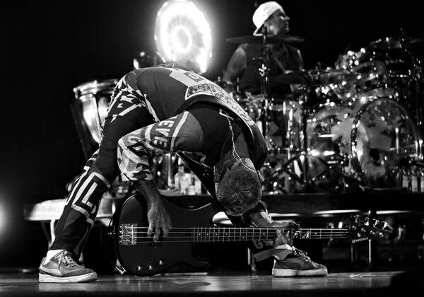 Musician bending over bass guitar on stage.