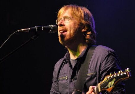 Musician singing and playing guitar on stage.