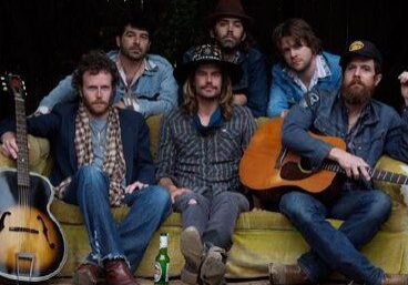 Band sitting with guitars on outdoor couch.