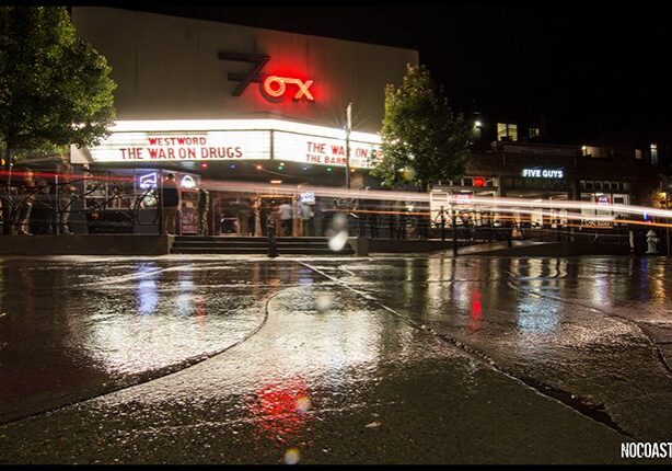 Wet street reflecting lights of theater marquee.