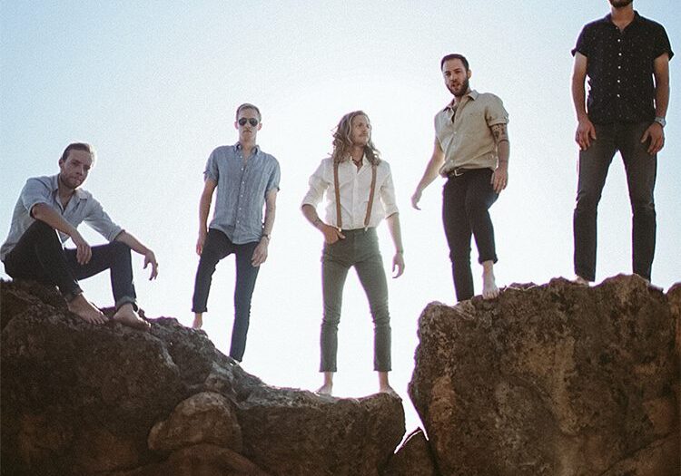 Band standing on rocks under blue sky.