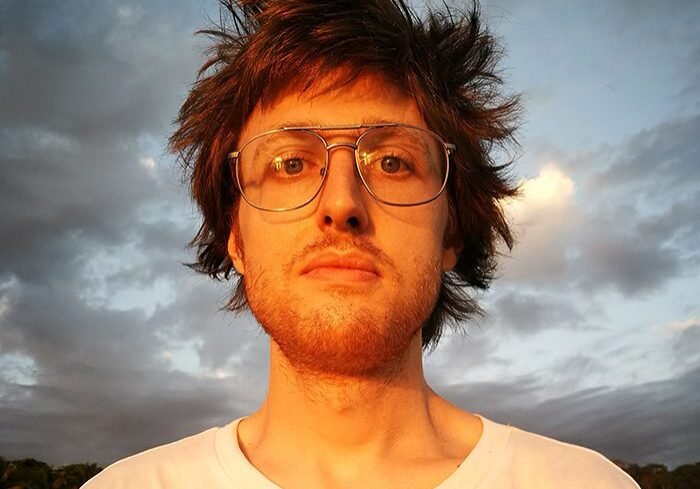 Man with glasses under cloudy sky.